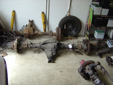 1993 Ford Bronco - Vehicle axles and shocks are stored on a garage floor next to a spare tire and battery display.