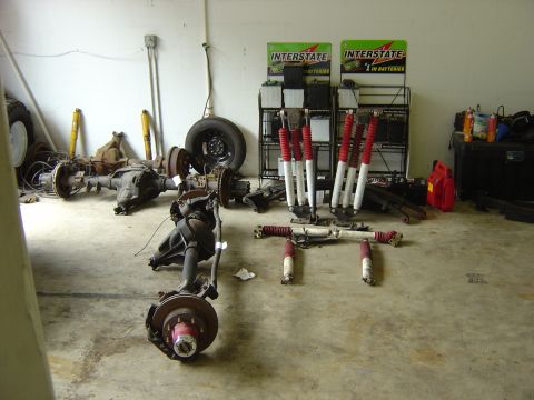 1993 Ford Bronco - A collection of vehicle axles and shock absorbers are stored indoors, with battery displays visible in the background.
