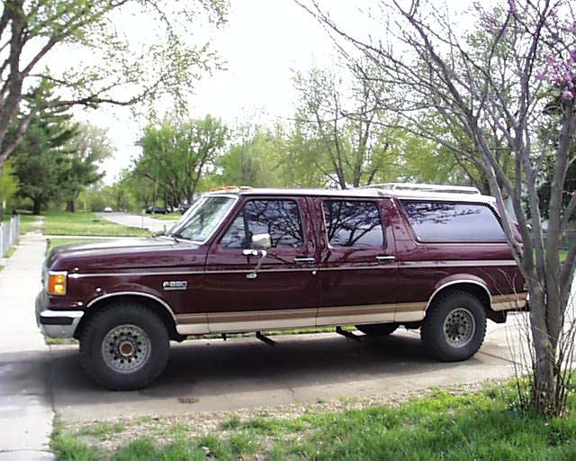 Maroon extended SUV conversion, side view, parked on driveway among trees