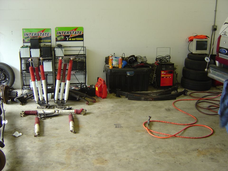 Shop floor with removed red-booted shocks, leaf springs and axle beside Interstate battery racks