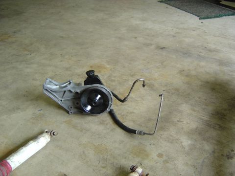 1993 Ford Bronco - A disassembled power steering pump and associated hoses are shown on a garage floor next to a shock absorber.