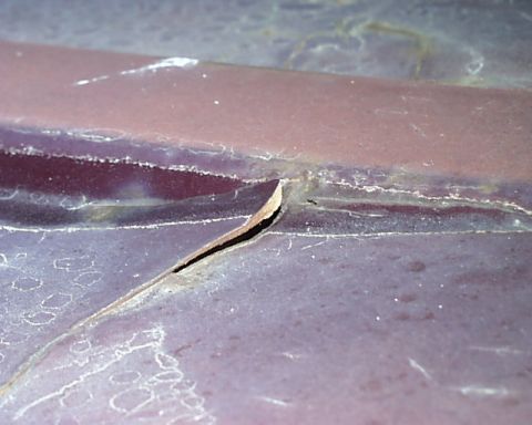 1988 Ford C-350 (Centurion Conversions) - Close-up of a cracked and peeling metal panel, showing signs of damage and wear.