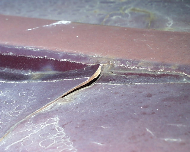 Close-up of cracked maroon paint and filler along a body-line seam