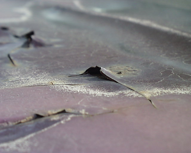 Close-up of cracked, peeling lavender-gray paint flaking off a body panel