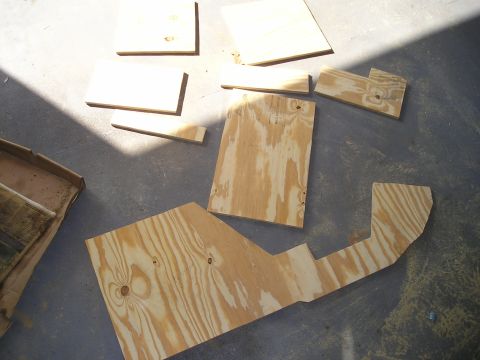 1996 Ford Bronco - Various custom-cut plywood pieces are arranged on a concrete floor, likely for a vehicle's center console project.