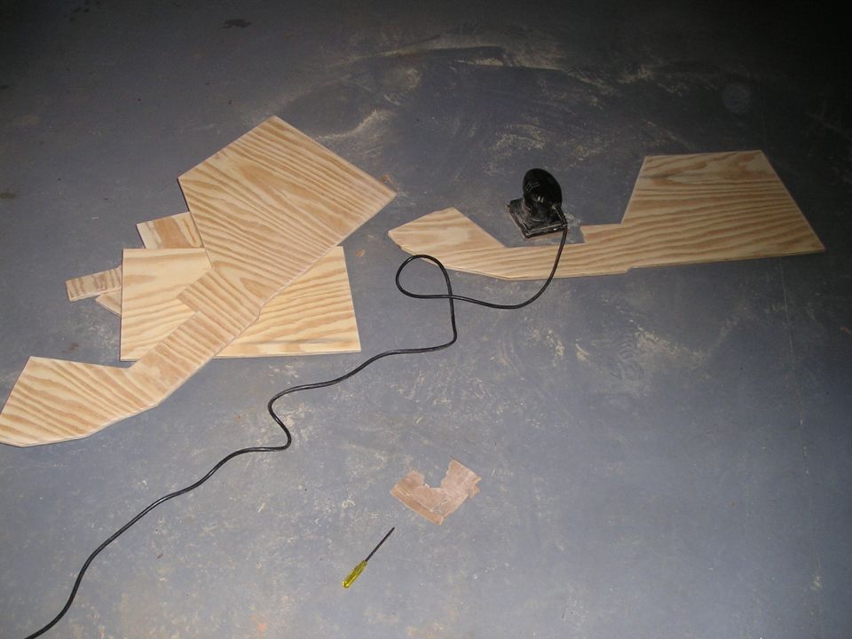 Cut plywood pieces, electric sander, and screwdriver on a concrete floor