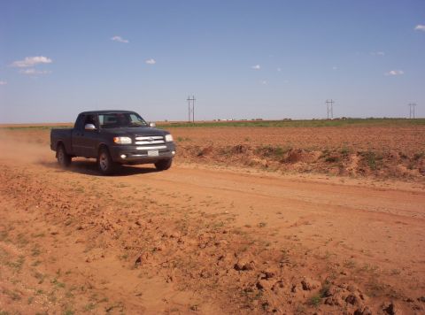 1988 Ford Bronco - A Toyota Tundra drives down a dusty rural road under a clear blue sky.