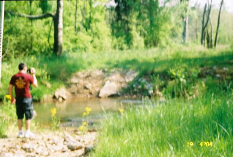 1988 Ford Bronco - A man stands by a stream in a grassy, wooded area.