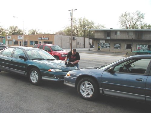 Green 1995 Dodge Intrepid and blue sedan parked, man leaning on hood