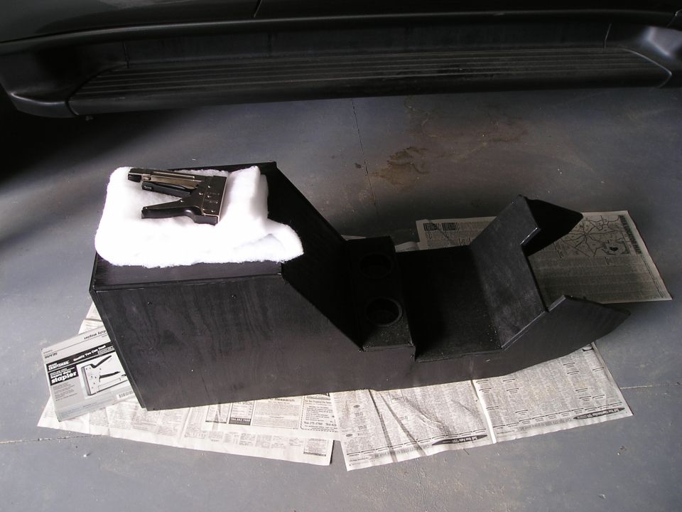 Custom black wood center console being built on newspaper with staple gun and batting