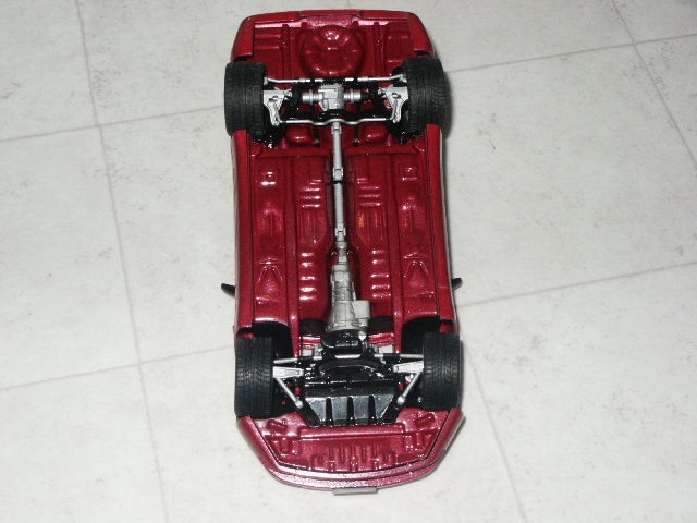 Underside view of a red model car showing the drivetrain and suspension components