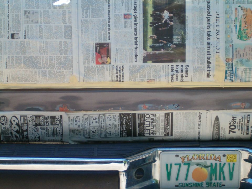 Rear of a vehicle with newspaper taped to the tailgate for protection during repair. Florida license plate visible