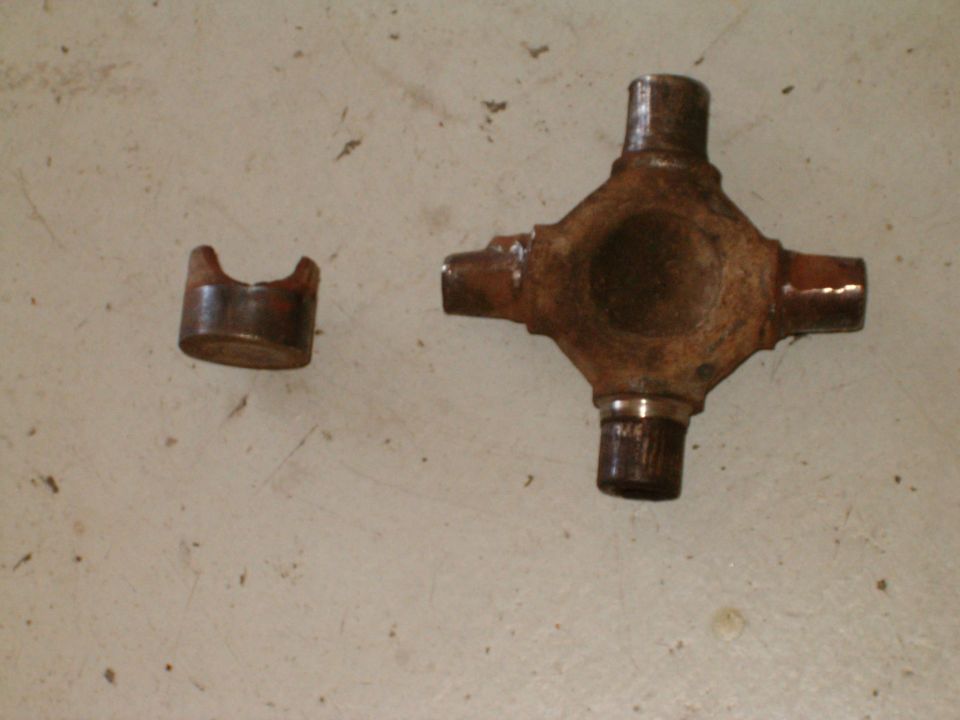 Rusty universal joint cross and one bearing cap on a light surface
