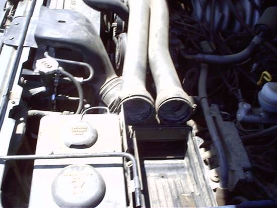 Engine bay with twin intake hoses, battery, and coolant reservoir under the hood