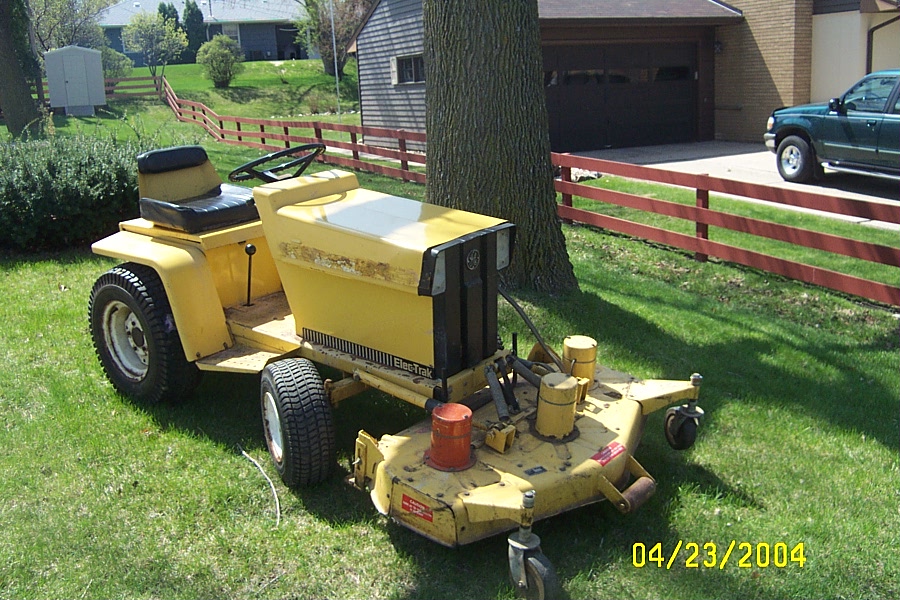 Yellow ElecTrak riding lawn mower with front mowing deck parked on grass near a tree.