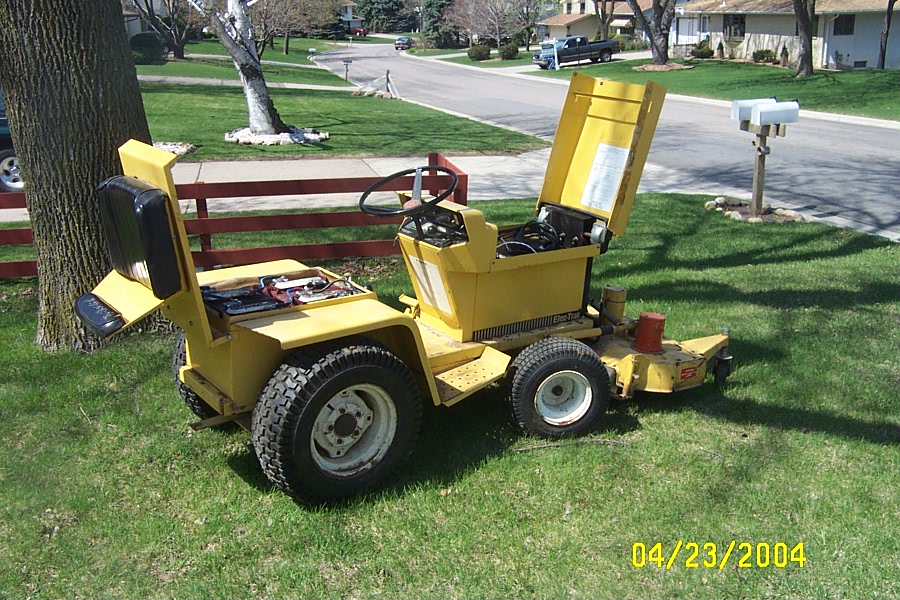 Yellow garden tractor with mower deck, hood and seat raised showing wiring, parked on a lawn; dated 04/23/2004.