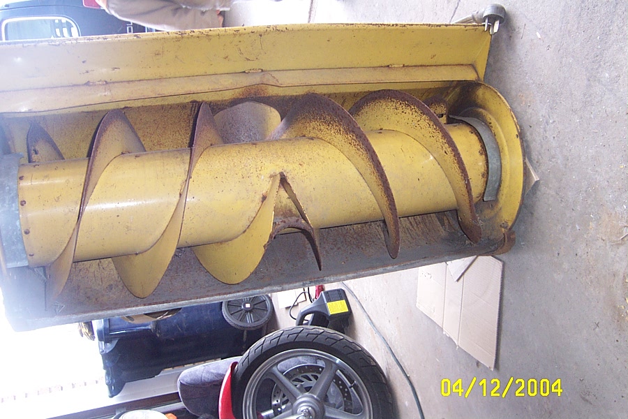 Yellow snowblower auger assembly removed and resting in a garage
