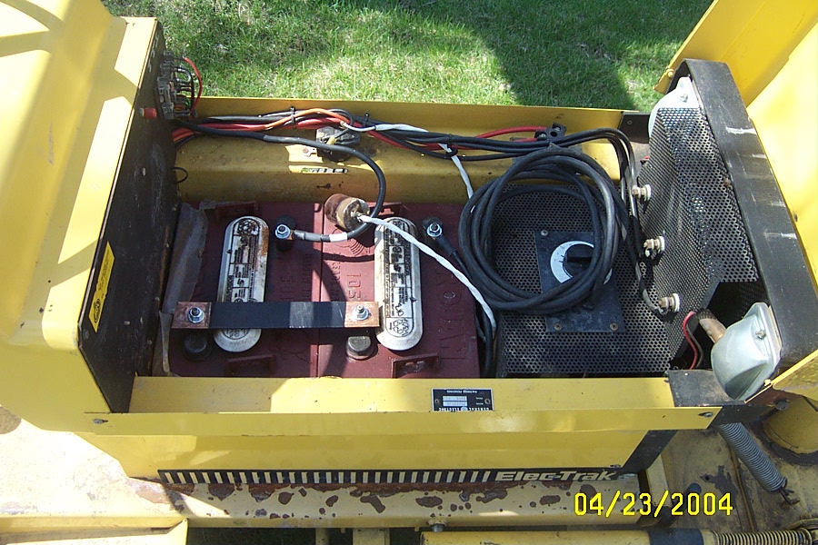 Open battery/electronics compartment of a yellow Elec-Trak electric tractor with red batteries and wiring