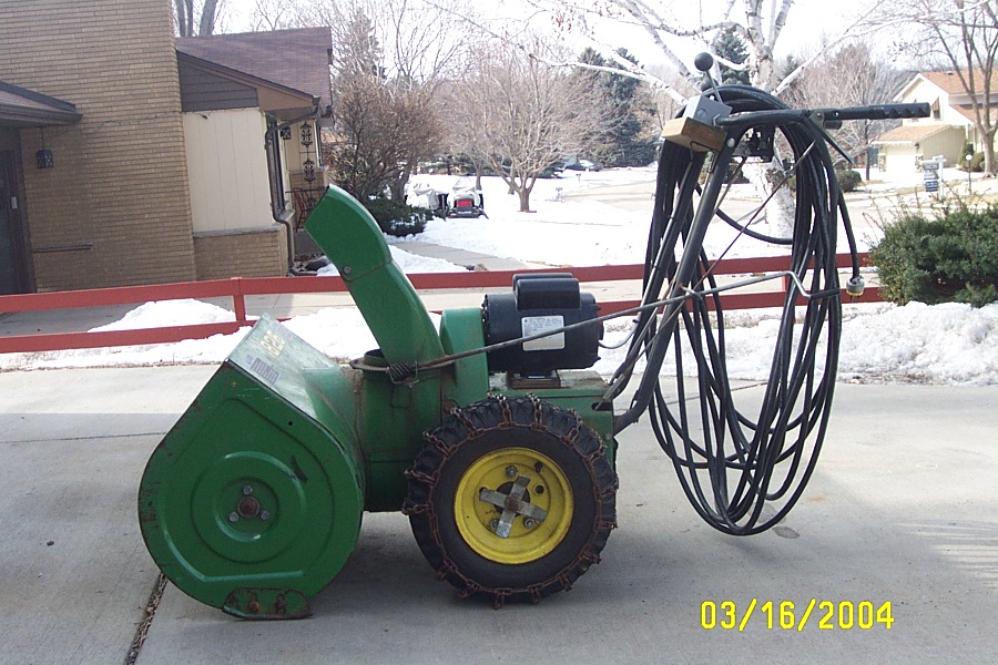 Green snowblower with electric motor and coiled cord on a snowy driveway, dated 03/16/2004