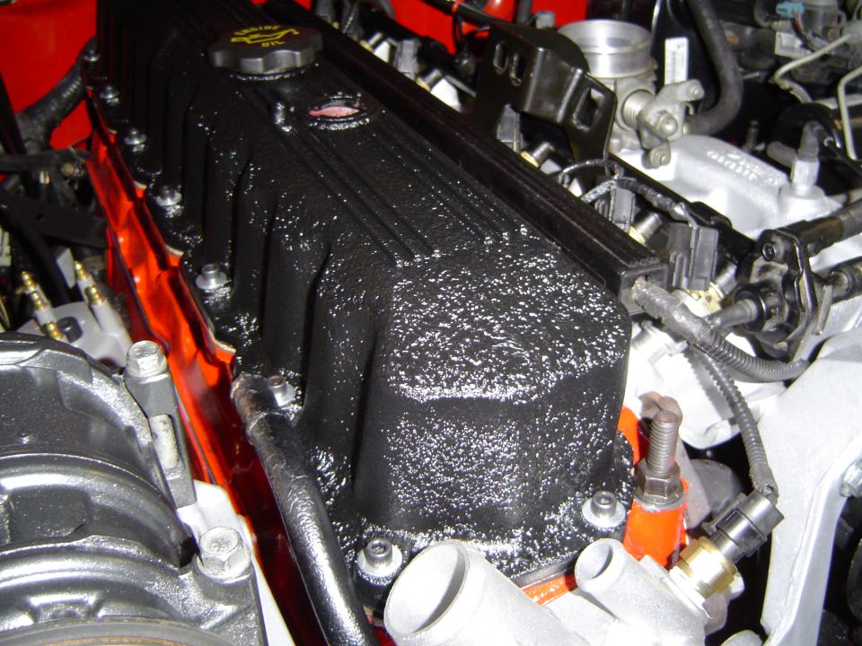 Black valve cover on an engine surrounded by red block and intake hardware