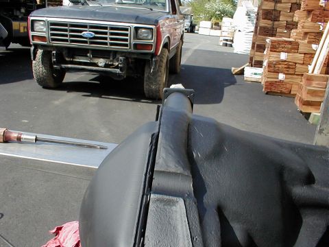 1983 Ford Bronco - Close-up along a black-painted axle housing showing the differential casting, welded truss seam and pinion snout, with a lifted red and bla…