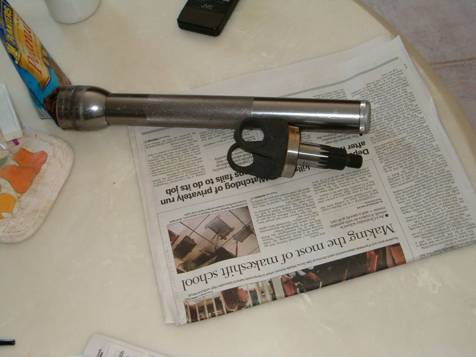 Maglite flashlight and a splined shaft with a black plastic connector on top of a newspaper
