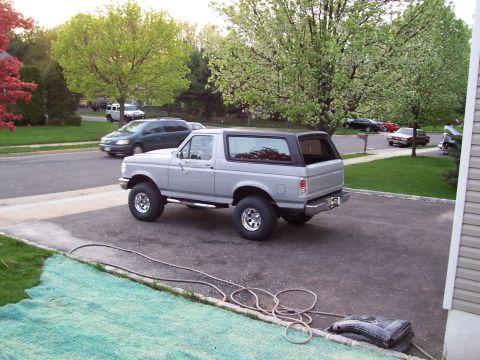 1990 Ford Bronco - Silver Ford Bronco with a black top is parked on an asphalt driveway in front of a house.