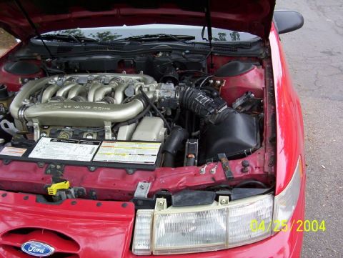 1995 Ford Taurus - The engine bay of a red 1995 Ford Taurus, showing the V6 engine and various components.