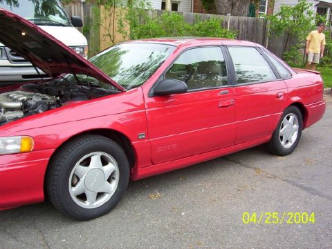 1995 Ford Taurus - Red 1995 Ford Taurus sedan with hood open, parked on a residential street.