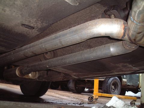 1967 Ford Galaxie - Dual exhaust system components visible from underneath a vehicle, with a jack stand present.