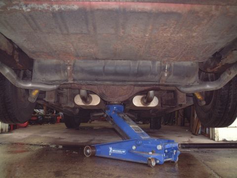 1967 Ford Galaxie - The underside of a vehicle is shown, supported by a jack, revealing the fuel tank and exhaust system.