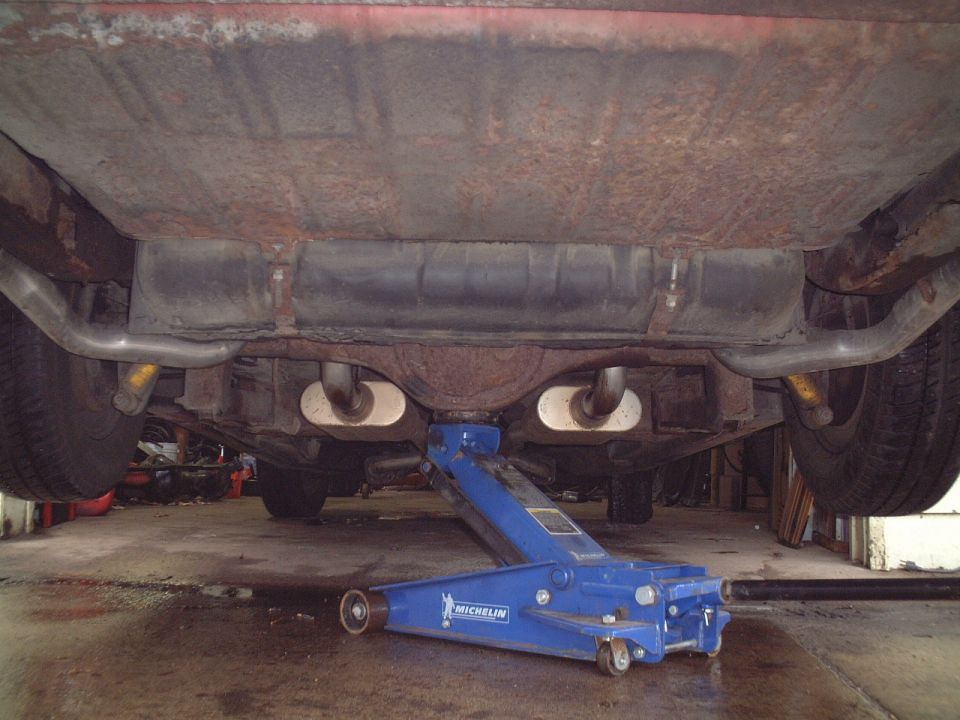 Vehicle undercarriage with dual exhaust and blue Michelin floor jack in garage