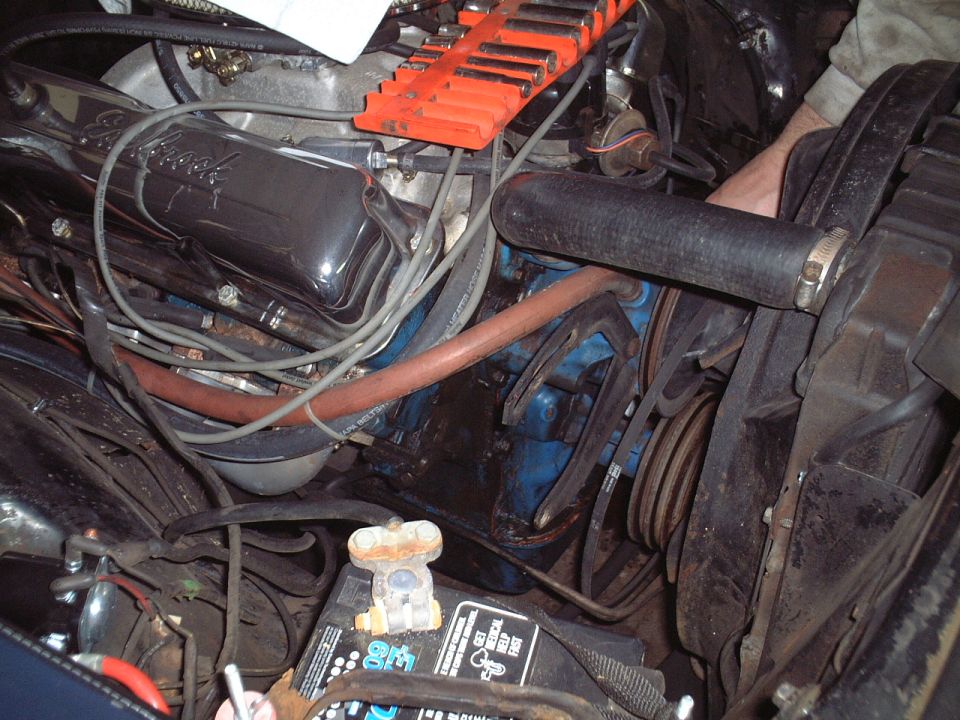 Engine bay with black Edelbrock valve cover, orange intake, radiator hose and belts