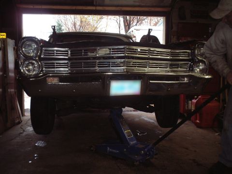 1967 Ford Galaxie - A car is raised on a jack in a garage, showing its front grille and headlights.