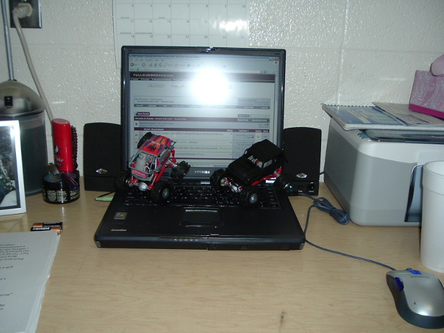 Two RC toy trucks sitting on a laptop keyboard with a web forum on screen