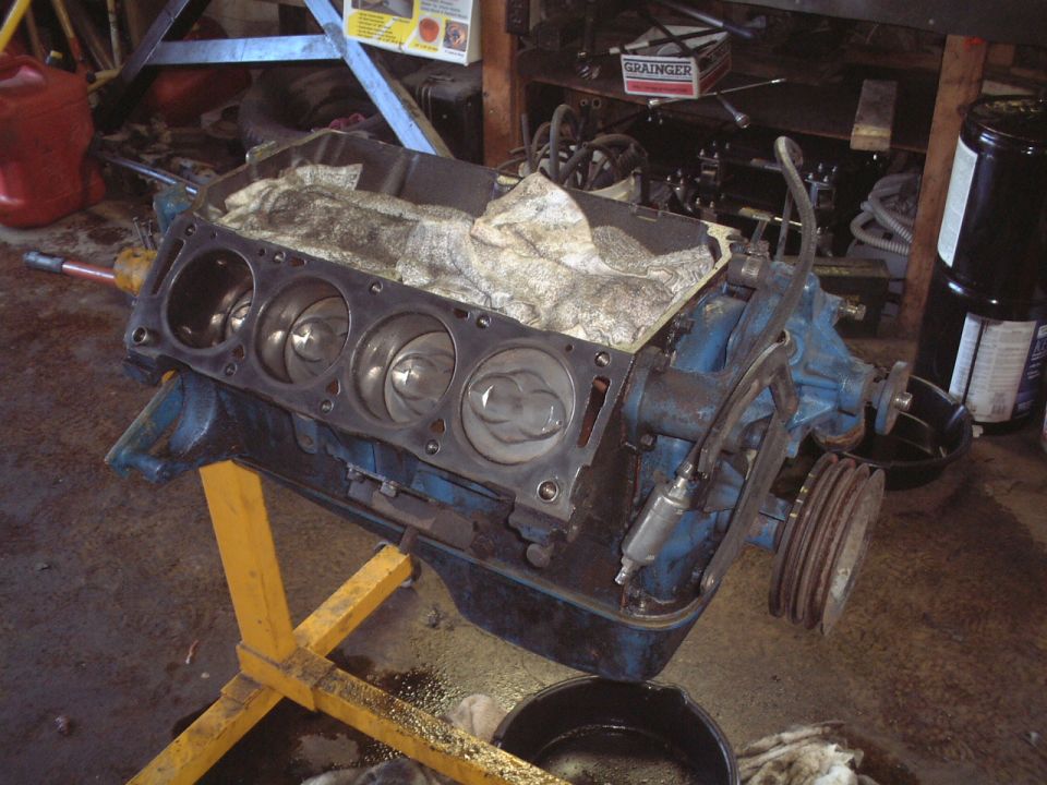 V8 engine block on yellow stand in garage, cylinder heads off exposing pistons