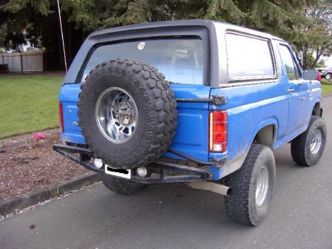 1980 Ford Bronco - The rear of a blue 1980 Ford Bronco is shown with a spare tire mounted on the tailgate and an aftermarket bumper.