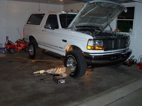 1994 Ford Bronco - A white 1994 Ford Bronco is parked in a garage with its hood up, and some parts are laid out on the floor.