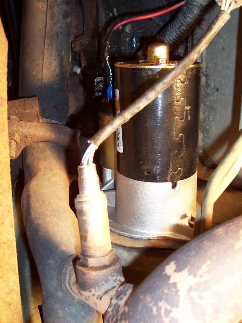 1994 Ford Bronco - Close-up view of a starter motor and oxygen sensor, showing electrical connections and exhaust components.