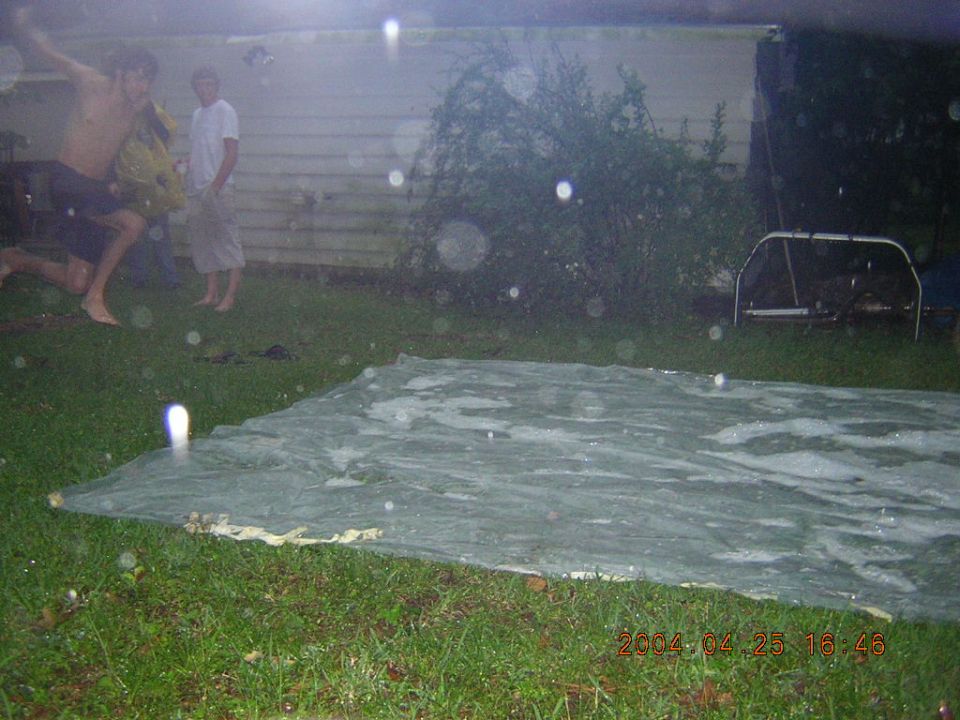 Two people playing on a slip 'n slide in a backyard
