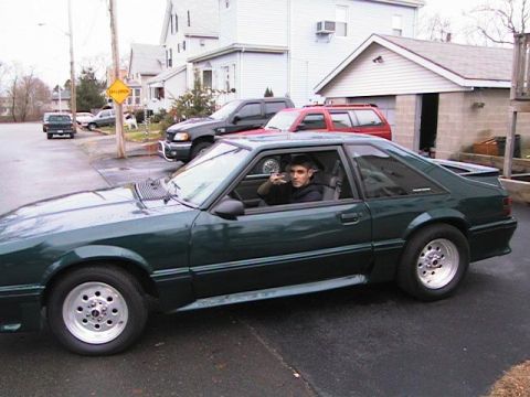 2000 Jeep Liberty - A green 1987 Ford Mustang coupe is parked on a street with houses and other vehicles visible.