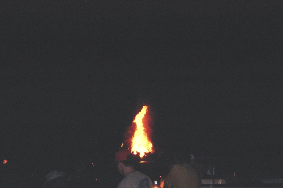 Bonfire erupting from the roof of a dark vehicle at night
