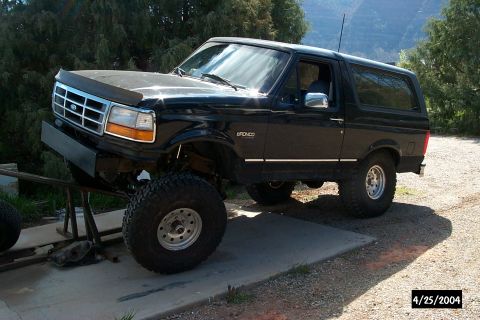 1996 Ford Bronco - A black two-door Ford Bronco full-size SUV shown from a 3/4 front angle with a lift kit and oversized off-road tires on chrome wheels, its…