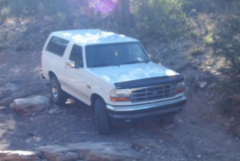 1995 Ford Bronco - White 1995 Ford Bronco navigating an off-road path with rocky terrain.