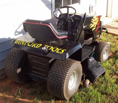 1979 Ford Bronco - Riding lawnmower with 'Binford Tools' branding, parked on grass near a building.