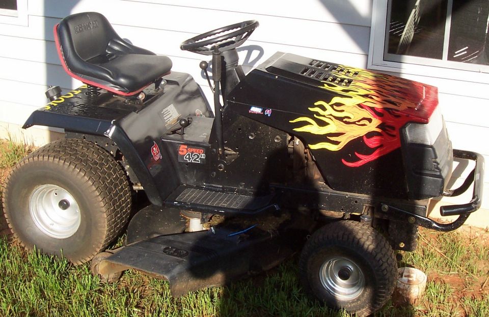 Black riding mower with flame decals on the hood. It has a black seat with red trim and large rear tires
