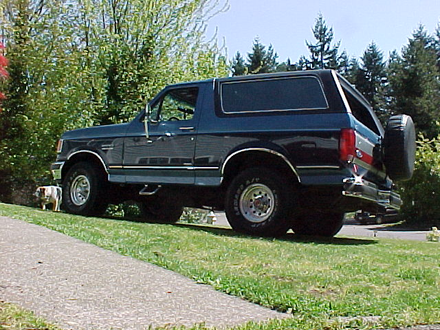 Blue lifted Ford Bronco full-size SUV parked side-on in a grassy yard