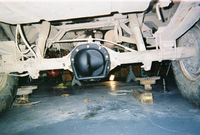 Rear axle and black differential cover under a lifted 4x4 raised on jack stands in a garage
