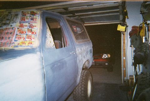 1983 Ford Bronco - A Ford Bronco is parked in a garage, prepped for paint with its windows covered by sale flyers.