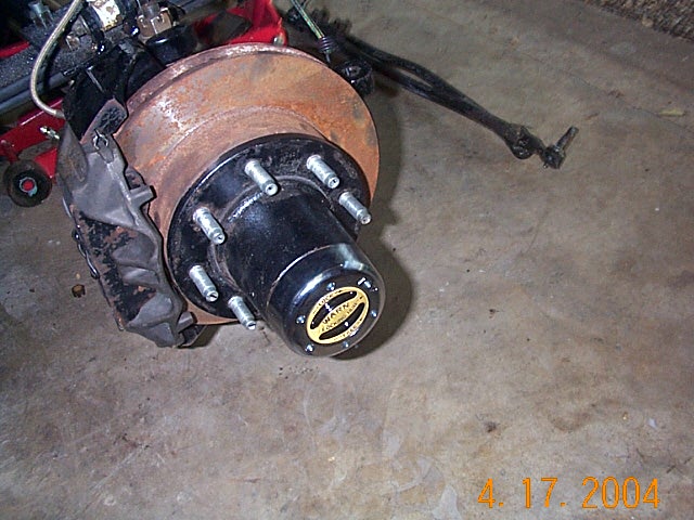 Front axle hub with black locking hub and rusty rotor on garage floor